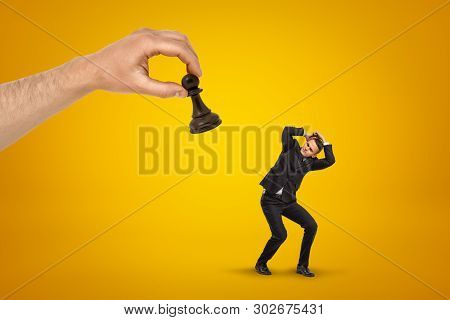 Little Scared Businessman Covering His Head With Hands To Protect From Huge Hand Holding Black Chess
