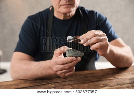 Male Jeweler Evaluating Semi Precious Gemstone At Table In Workshop, Closeup