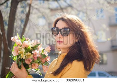 Female Portrait Of Sensual Brunette Woman In Dark Sunglasses And Yellow Jacket Holding A Big Bouquet
