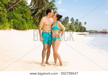 Young Couple Standing On Beach Kissing Near The Coast