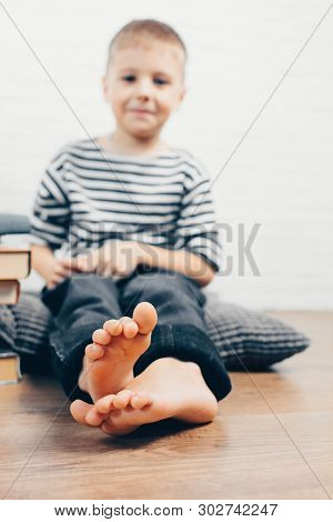 Boy Sitting On The Floor At Home And Smiling. Concept Of Healthy Feet, And Flat Feet Treatment.  Unf