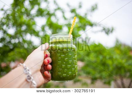 woman's hand holding a jar with green cold-pressed juice, nature background. Healthy eating, detoxing, juicing, body cleancing concept 