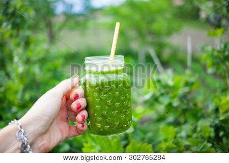 woman's hand holding a jar with green cold-pressed juice, nature background. Healthy eating, detoxing, juicing, body cleancing concept 