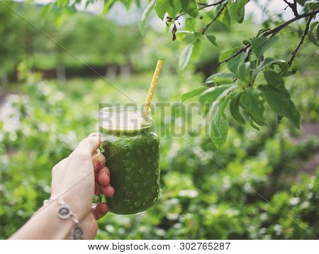woman's hand holding a jar with green cold-pressed juice, nature background. Healthy eating, detoxing, juicing, body cleancing concept 