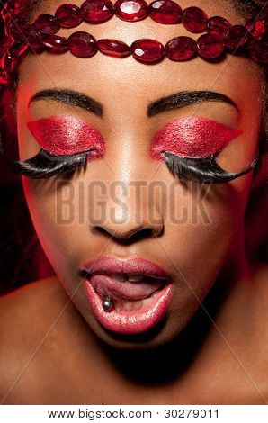 Närbild av en afrikansk kvinna bära pärlor runt hennes panna och kreativa magenta makeup. Hon har h