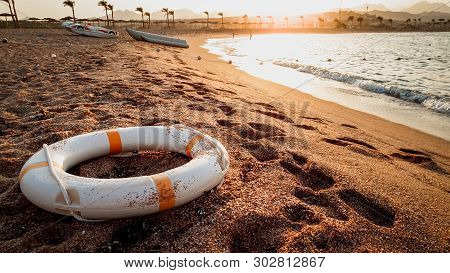 Closeup Toned Image Of Life Saving Ring Lying On The Sea Baech Sand. Beutiful Sunset Over The Ocean