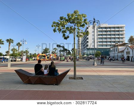 Larnaka, Cyprus - May 11, 2019: Family Sitting On A Bench On The Promenade Phinikoudes Near The Sea