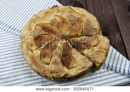 Apple Pie Strudel In A Baking Dish With A Cut Piece Of Cake On A Wooden Table With A Blue Striped Na