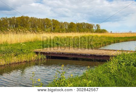 Simple Wooden Bridge With Steel Beams Over A Winding Stream In The Dutch Nature Reserve Kornsche Boe