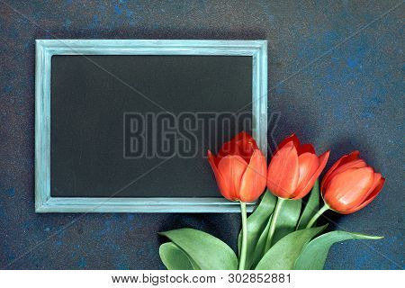 Blackboard And Bunch Of Red Tulips On Abstract Dark Background, Space For Your Test. Flat Lay, Toned