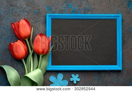 Blackboard And Bunch Of Red Tulips On Abstract Dark Background, Space For Your Test. Flat Lay, Toned