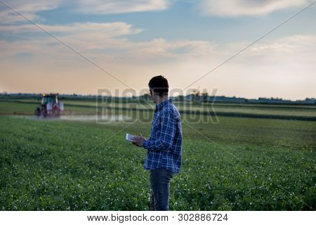 Young Attractive Farmer With Tablet Standing In Front Of Tractor In Field