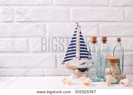 Nautical Or Marime Decorations Near By White Brick Wall. Decorative Boat Or Ship, Blue Bottles With 