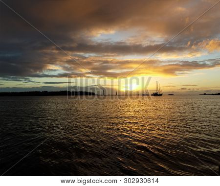A Vibrant Nautical Golden-yellow Coloured Nimbostratus Cloudy Sunrise Seascape Over Sea Water With W