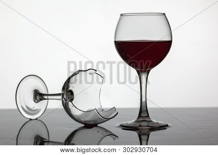 Filled With A Glass Of Wine And Broken Wine Glass With Red Wine Which Is Laying On The Wet Surface. 