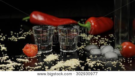 Pouring Vodka Into Shot Glasses Which Are Placed On A Black Surface With Pepper, Sesame And Cherry T