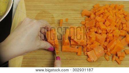 Female Housewife Hands Slicing Carrots Into Pieces On The Wooden Cutting Board In The Kitchen