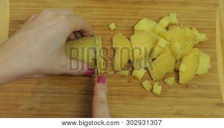 Female Housewife Hands Slicing Potatoes Into Pieces On The Wooden Cutting Board In The Kitchen