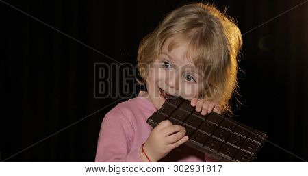 Attractive Child Eating A Huge Block Of Chocolate. Cute Blonde Girl Bite A Chocolate. Brown Eyes. Pr