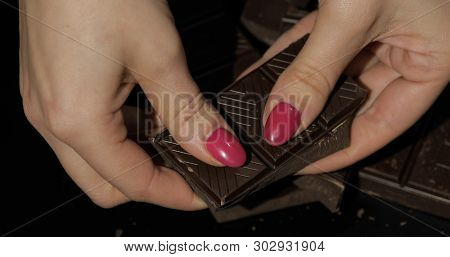 Woman Holds Black Chocolate Bar. Close-up Shot Of Woman Fingers With The Chocolate