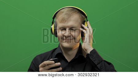 Guy Listens To Music In Wireless Yellow Headphones. Portrait Of Attractive Man Using Smart Phone For