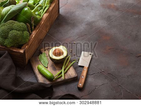 Assorted Green Toned Raw Organic Vegetables In Wooden Box On Dark Stone Background. Avocado, Cabbage