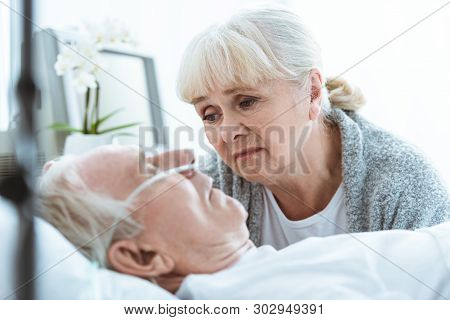 Sad Senior Woman Looking At Husband In Coma In Clinic