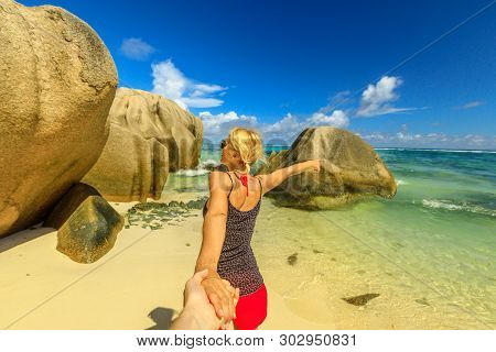 Follow Me. Blonde Tourist Woman Holding Hand Of Her Partner At Seychelles. Beautiful Anse Source Dar