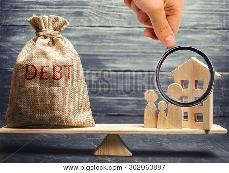 Money Bag With The Word Debt And A Miniature House With A Family On The Scales. Payment Of Debt For 