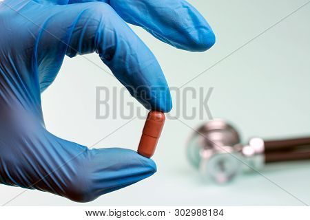 Scientist  Holding A Pill With Fingers In Blue  Glove.  Painkillers And  Prescription Drugs And Hydr