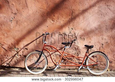 Modern Comfortable Orange Tandem Double Bicycle With White Wheels On Paved Empty Sidewalk Leaned Aga