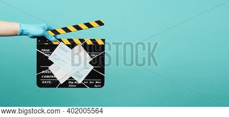 Hand Is Wear Madical Glove And Hold Black Clapper Board Or Movie Slate With Face Masks. It Use In Mo