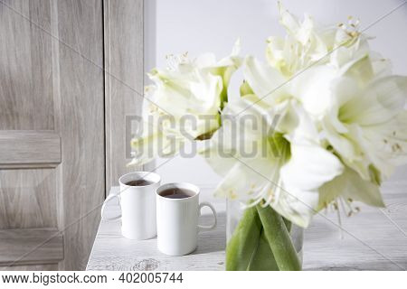 Bouquet Of White Lilies In A Tall Glass Vase On A Beige Table Against A Gray Wall. Copy Space