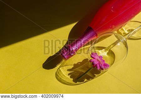 Festive Party Concept. Hard Light Hard Shadows. Glass And Bottle Of Pink Champagne On A Yellow Backg