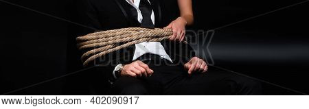 Cropped View Of Dominant Woman Holding Rope On Tied Submissive Man Sitting On Black, Banner