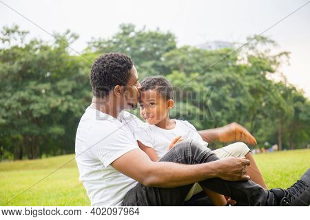 Happy African American Father While Hug And Carry His Son, Dad Was Kissing His Son In The Park, Joyf