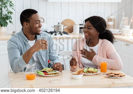 Young Happy Black Couple Having Healthy Breakfast Together In Kitchen At Home, Eating Toasts And Dri