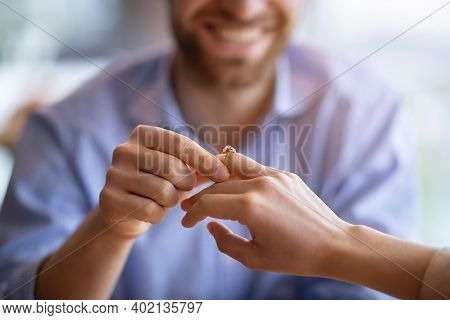 Happy Guy Holding His Fiancees Hand, Putting On Engagement Ring On Her Finger, Closeup View. Unrecog