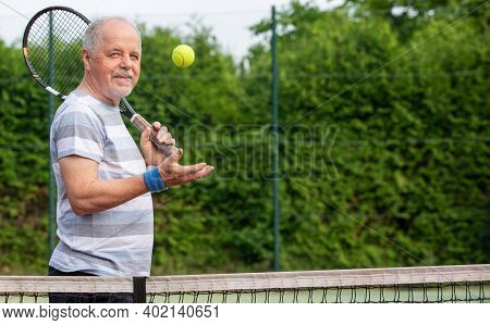 Portrait Of An Active Senior Man At The Tennis Court With Racket And Tennis Ball, Sport Concept