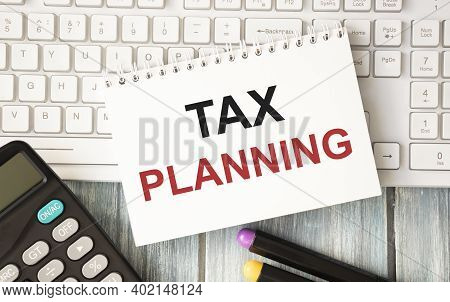 Notepad With Tax Planning Text On Keyboard With Felt-tip Pens And Calculator On Wooden Background.