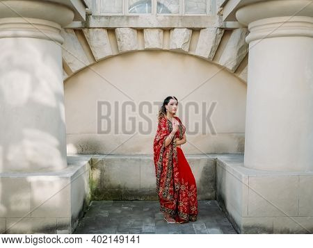 Young Beautiful Indian Woman Dancing In Red Sari On Background Walls Ancient Building Outdoors.