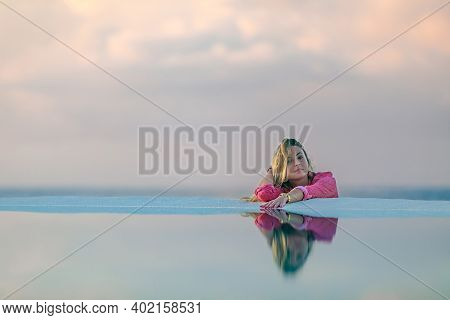 A Young Girl In A Red Shirt, At Dawn By The Sea Pool, Calm And Relaxed Looking At The Reflection In 
