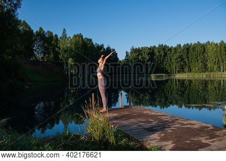 Young Woman Relaxing By The Lake At Sunset, Harms Outstretched. Doing Youga In The Morning At Forest