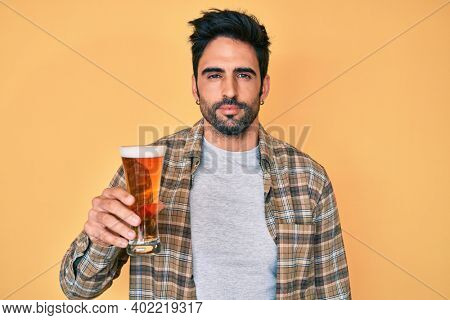 Handsome hispanic man with beard drinking a pint of beer thinking attitude and sober expression looking self confident 