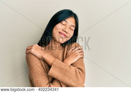 Young chinese woman wearing casual clothes hugging oneself happy and positive, smiling confident. self love and self care 