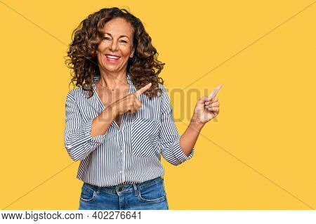 Middle age hispanic woman wearing casual clothes smiling and looking at the camera pointing with two hands and fingers to the side. 