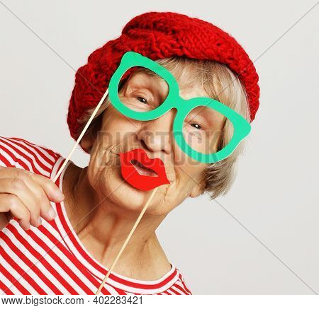 lifestyle, people and party concept: funny grandmother wearing red clothes holding falce glasses and ready for party