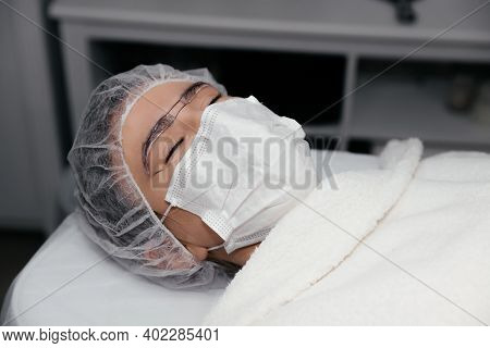 Close-up Of The Woman Face In Cap And Medical Mask With White Anesthetic Cream On The Eyebrows Befor