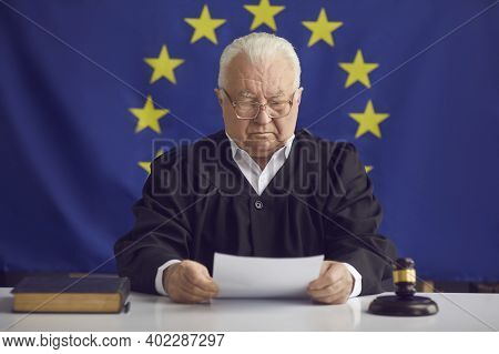 Serious Judge Reading Document While Sitting At Table Against Eu Flag Background