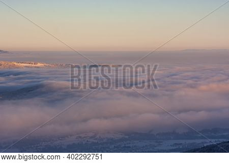 Wonderful View Of Snowy Landscape Covered With Fog And Clouds. The Setting Sun Is Staining The Sky.